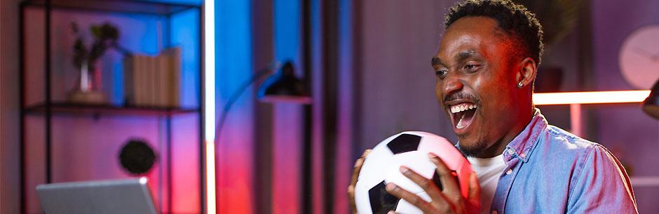 Man holding a soccer ball celebrates in front of his laptop