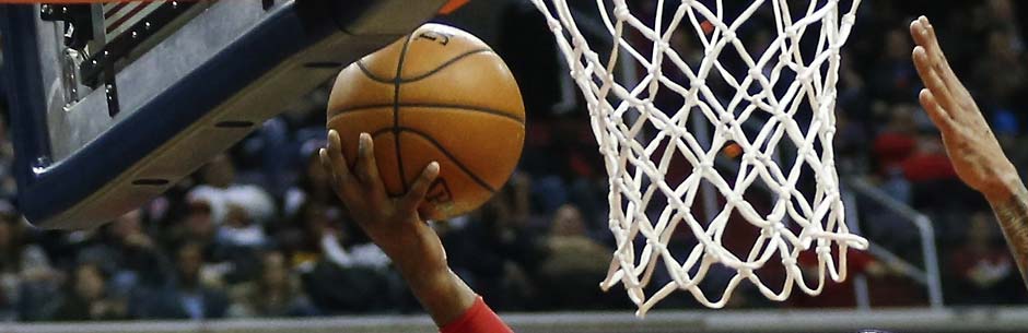 A basketball players lays the ball up at the basket